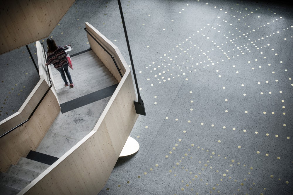 Reflekterande mässingspunkter i ett mönster, ingjutna i ett terrazzogolv, bredvid en trätrappa. Sophie Tottie, P.ULL