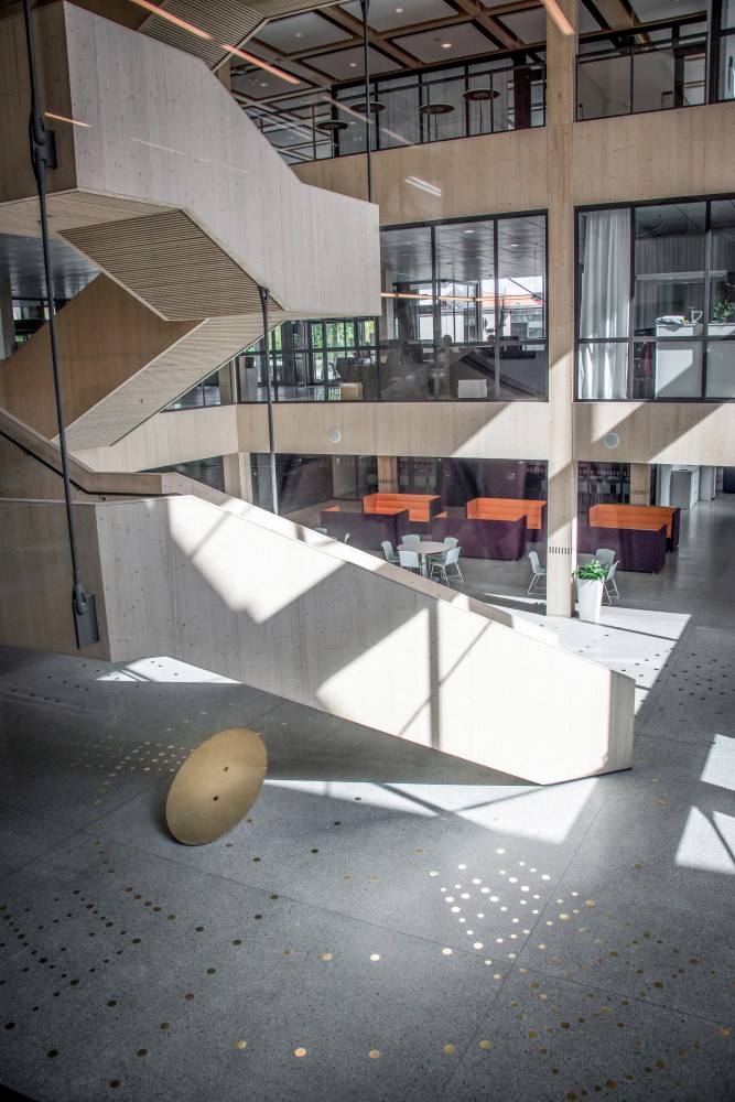 Reflekterande mässingspunkter i ett mönster, ingjutna i ett terrazzogolv, bredvid en trätrappa. I bakgrunden sittgrupper. Sophie Tottie, P.ULL
