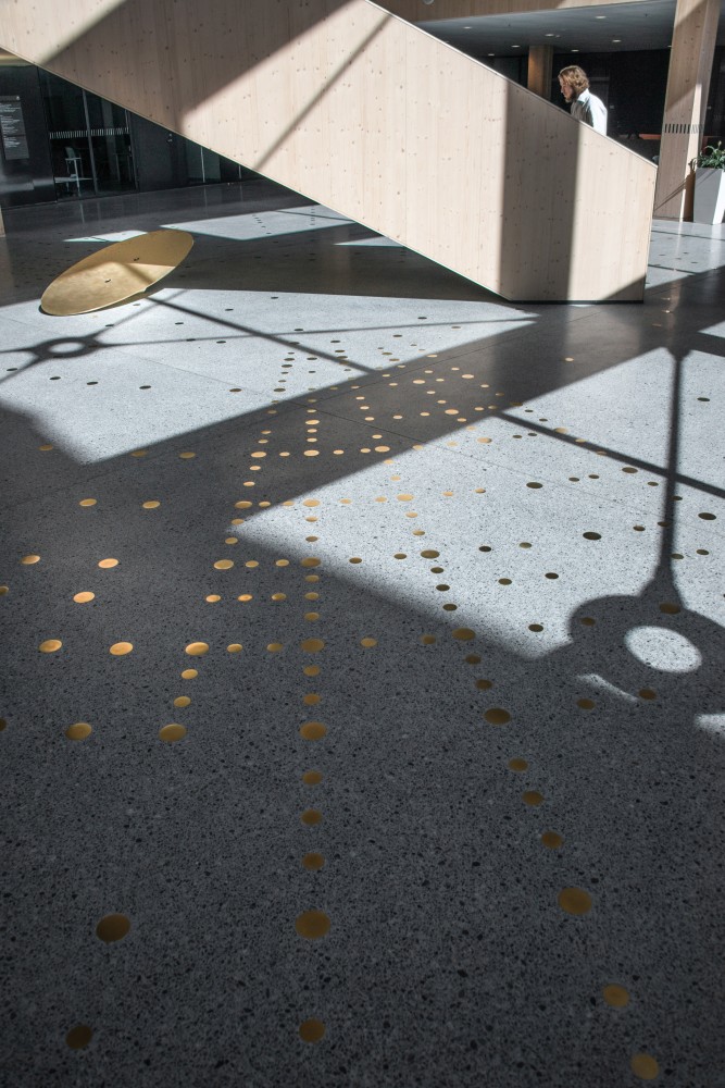 Reflekterande mässingspunkter i ett mönster, ingjutna i ett terrazzogolv, bredvid en trappa av trä. Sophie Tottie, P.ULL