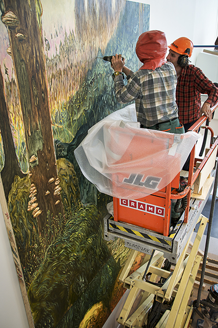 Två män med bygghjälmar i en skylift monterar överdelen av målningen på väggen. Danilo Stankovic, När fåglar tystna.