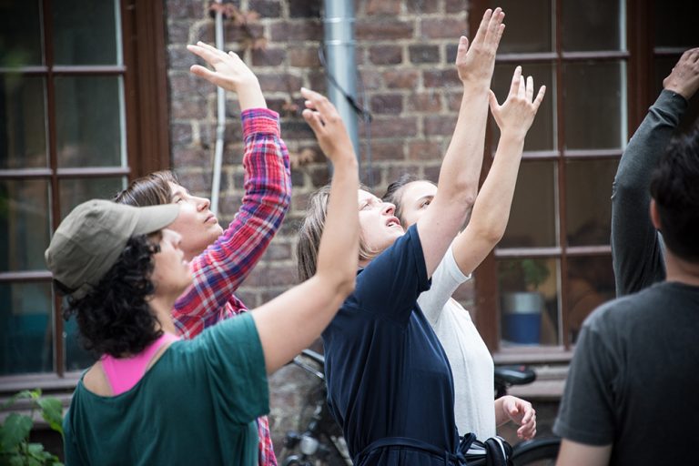 Fyra kvinnor står utomhus med höger hand lyft och blicked i handflatan. Myriam Lefkowitz, Walk, hands, eyes (Gamlegården)