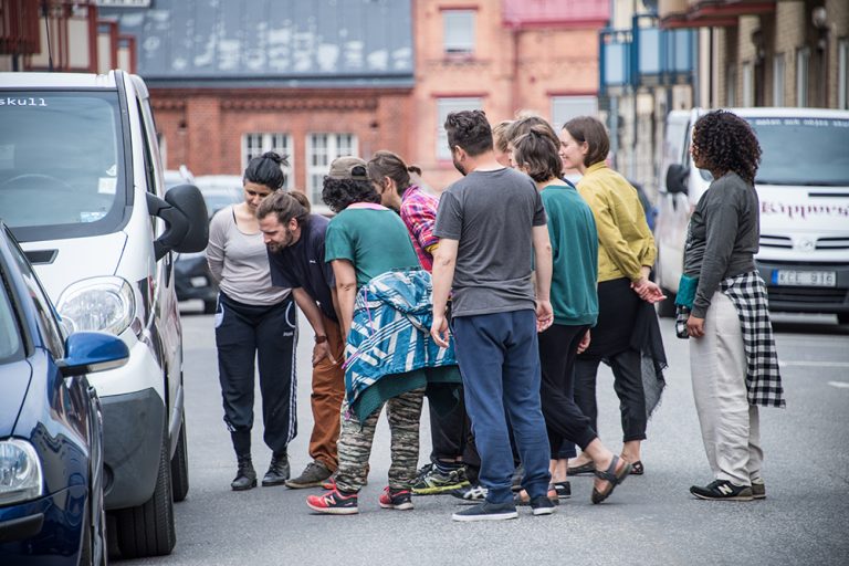 io personer står i en klunga på gatan och studerar karossen på en parkerad bil. Myriam Lefkowitz, Walk, hands, eyes (Gamlegården)