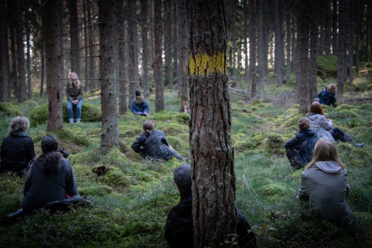 En grupp människor sitter på huk i en mossig och murrig skog
