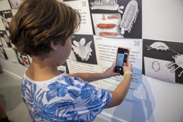 Ett barn scannar av en text som hänger på väggen med mobilen